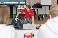 DRK-Ausbilder zeigt Teilnehmenden die stabile Seitenlage in einem Erste-Hilfe-Kurs