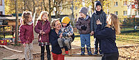 Kinder und Erzieherinnen lachen gemeinsam auf dem Spielplatz einer DRK-Kita