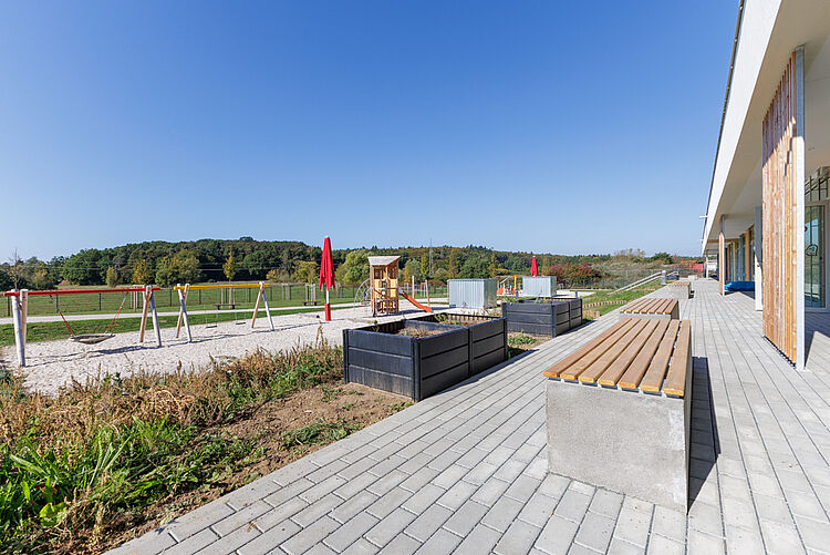 Gepflasterte Terrasse mit Sitzbank, Hochbeeten und Blick auf den Spielplatz