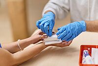 Person mit blauen Handschuhen legt einen Verband an einer Hand an