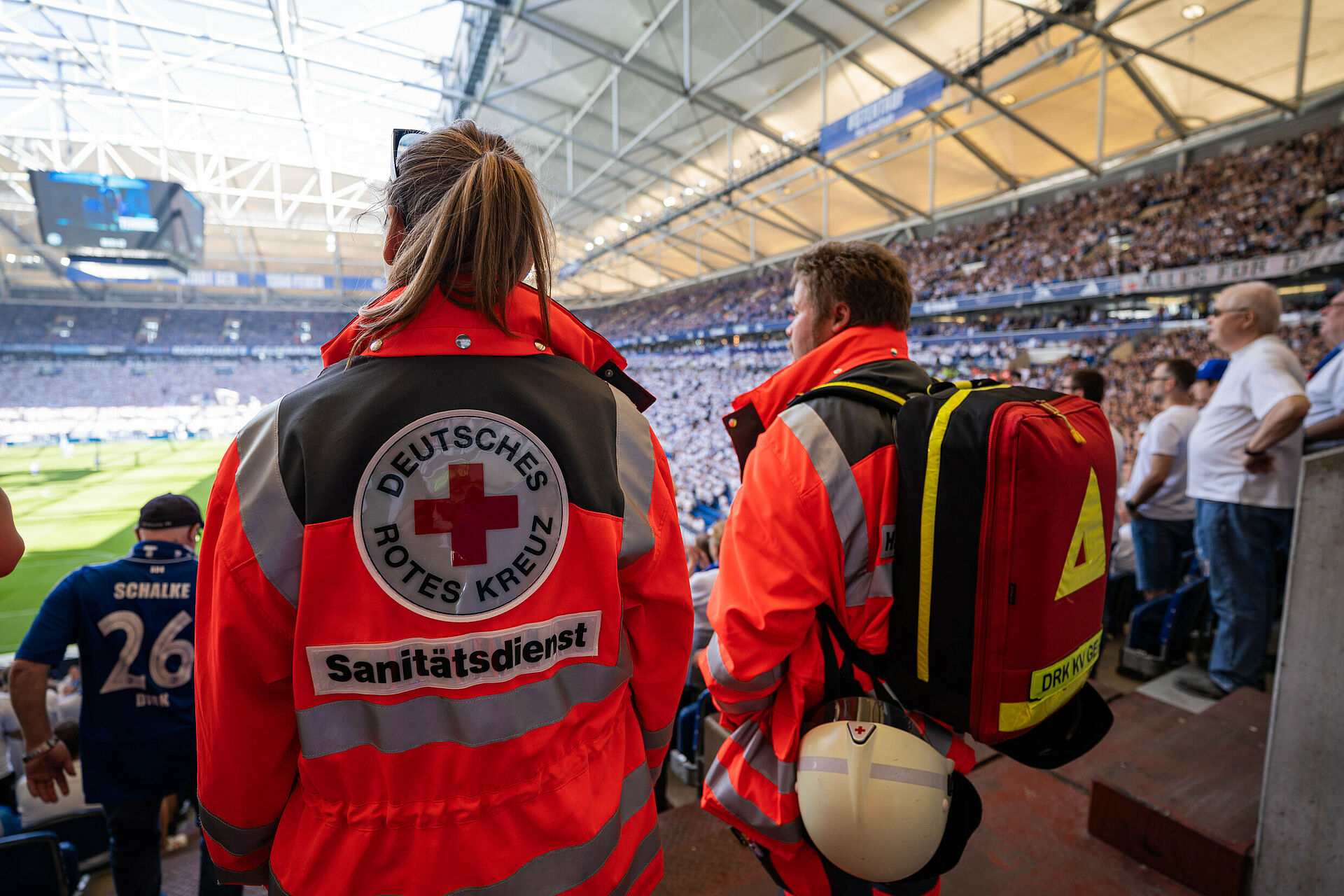 Zwei Einsatzkräfte des DRK-Sanitätsdienstes beobachten das Geschehen in einem vollen Stadion