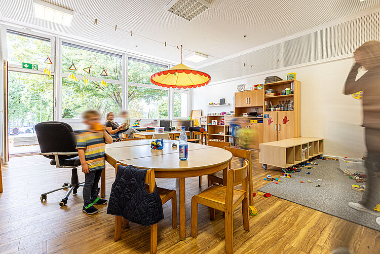 Kinder spielen mit Bausteinen und Spielsachen im Gruppenraum mit großen Fenstern