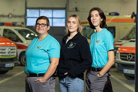 Die drei Leiterinnen des JRK Gießen 2 stehen in einer DRK-Fahrzeughalle: Rebecca, Natascha und Lejla.