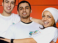 Gruppe fröhlicher Jugendlicher des Jugendrotkreuzes in weißen Shirts vor oranger Wand