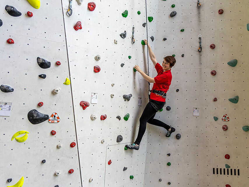 Frau klettert gesichert an einer hellen Kletterwand während eines therapeutischen Trainings