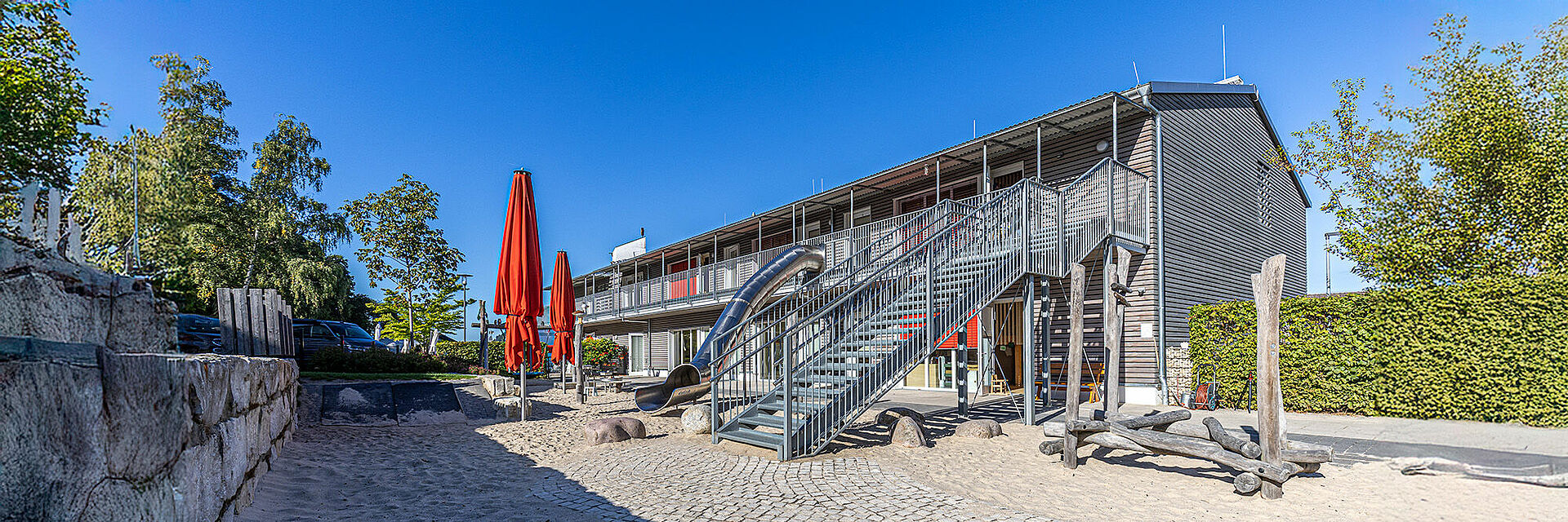DRK-Kita „Henrys kleine Forscher“ in Staufenberg-Daubringen – Moderne Kindertagesstätte mit Spielbereich Außenansicht der DRK-Kita „Henrys kleine Forscher“ in Staufenberg-Daubringen mit Spielplatz, Rutsche und Sonnenschirmen