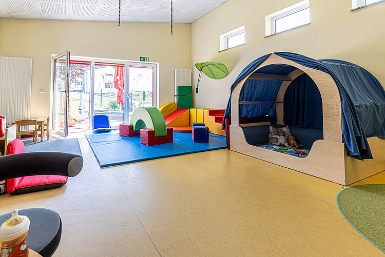 Heller Raum mit Bewegungsmatten, Kletterelementen und Spielhöhle