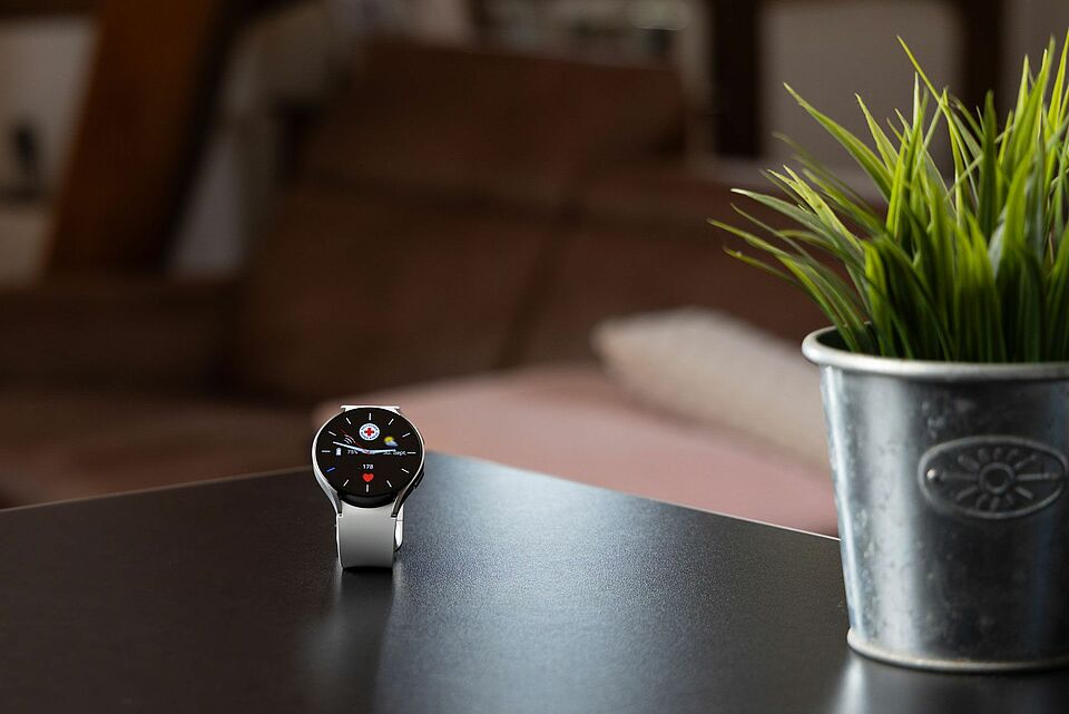 Moderne DRK-Mobilruf-Smartwatch mit Notruffunktion auf einem Tisch neben einer Pflanze