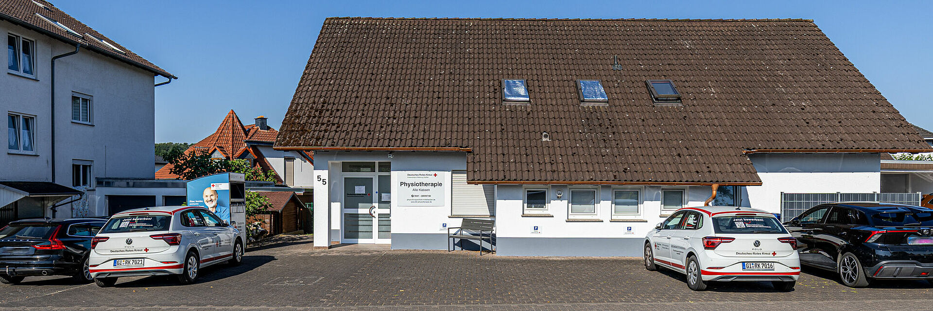 Eingangsbereich der DRK Physiotherapiepraxis in Pohlheim mit DRK-Fahrzeugen und Praxis-Schild