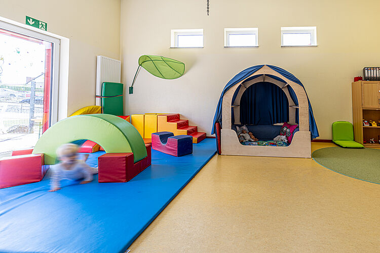 Kleinkindbereich mit bunten Bewegungselementen und Kuschelecke
