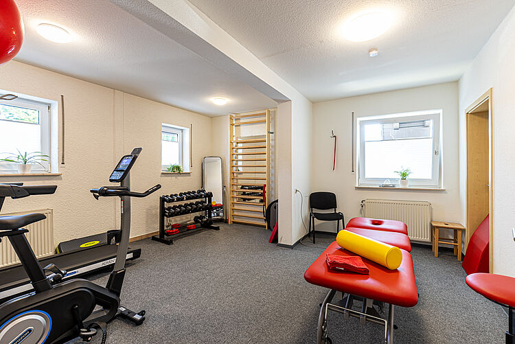 Trainingsraum mit roten Therapieliegen, Hanteln und Ergometer in der DRK-Therapiepraxis