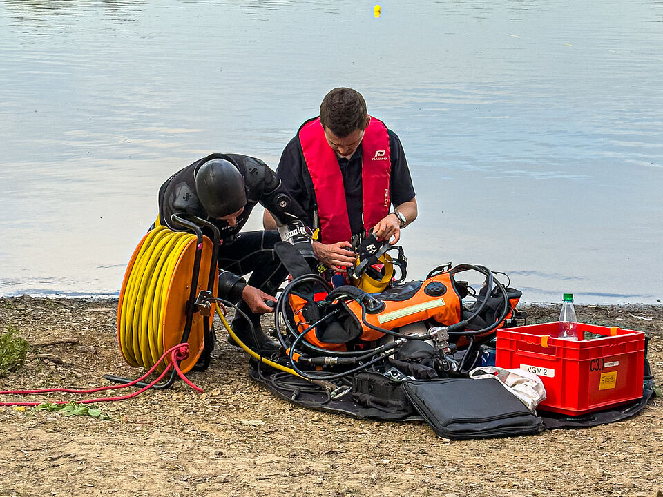 Zwei Mitglieder der DRK Wasserwacht prüfen Tauch- und Atemausrüstung am Ufer