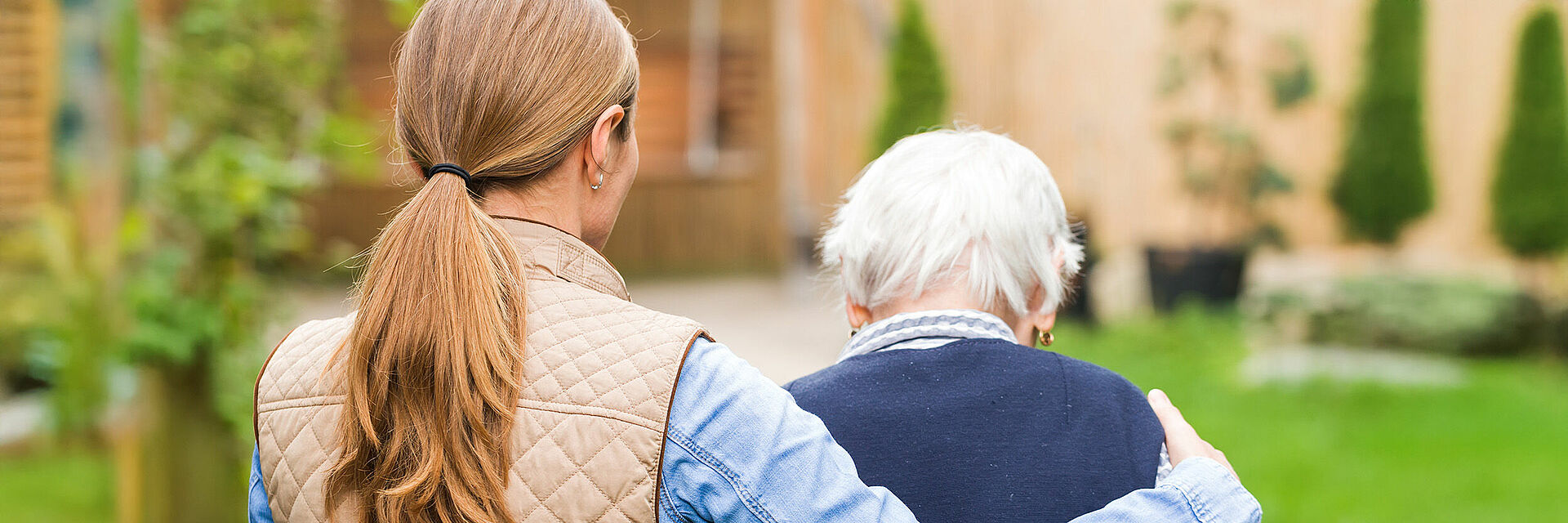 Jüngere Frau unterstützt Seniorin beim Gehen im Garten