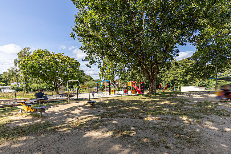 Kita-Spielplatz mit Klettergeräten und Schatten spendenden Bäumen