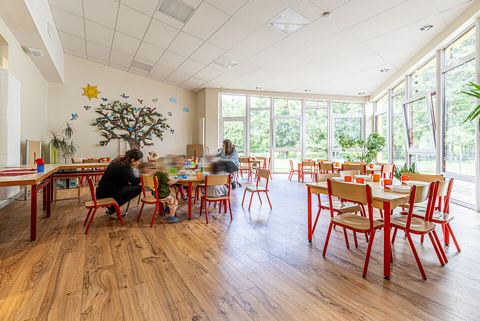 Kinder essen gemeinsam im hellen Speiseraum mit Wanddekoration und großen Fenstern