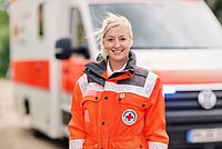 Lächelnde DRK-Notfallsanitäterin steht vor Rettungswagen
