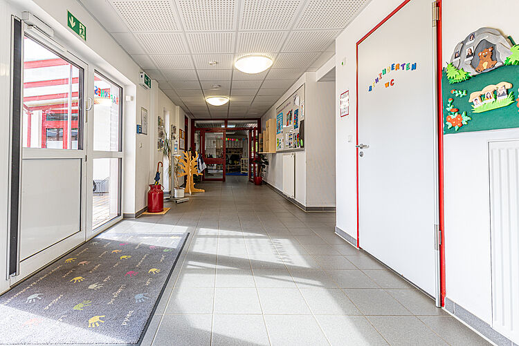 Blick durch den hellen Flur der Kita mit roten Türen und Wanddekorationen