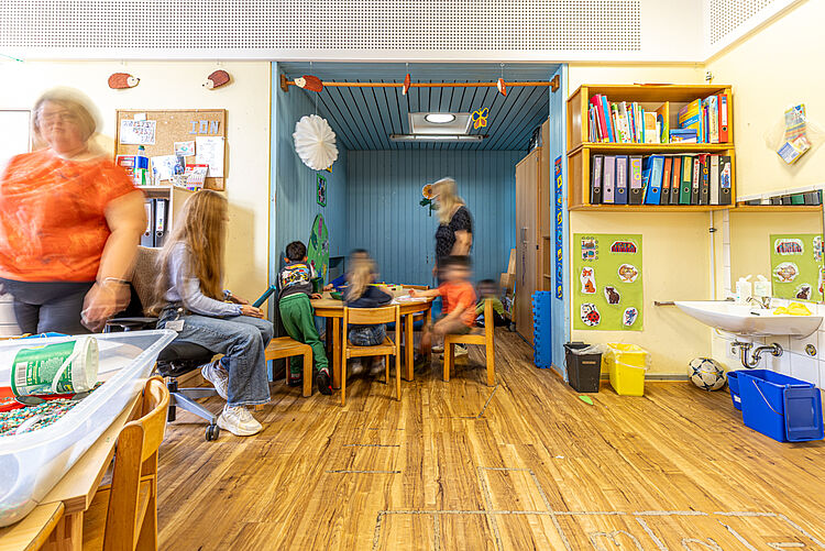 Kinder basteln und malen im Gruppenraum unter Begleitung von Erzieherinnen