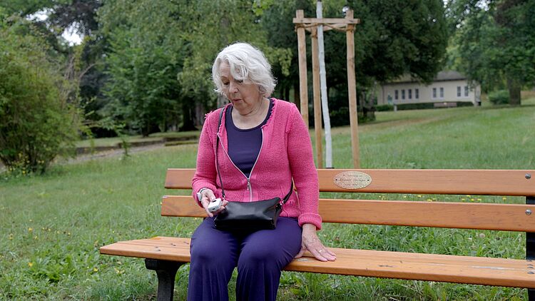 Seniorin drückt mobilen Notrufknopf auf einer Parkbank