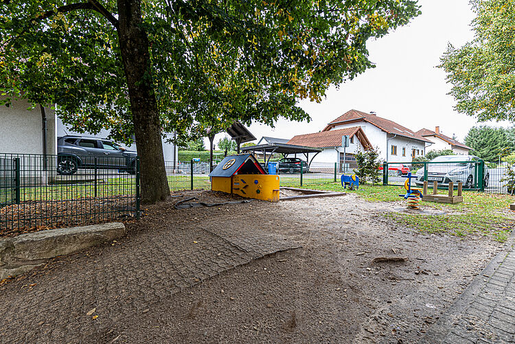 Sandkasten und Spielgeräte unter Bäumen bei der DRK-Kita Kunterbunt