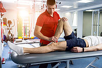 Physiotherapeut führt Mobilisationsübung am Bein eines Patienten in moderner Praxis durch
