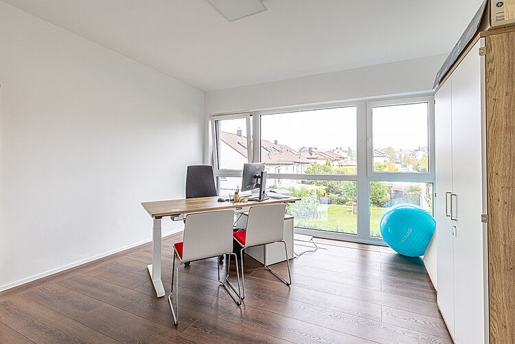 Heller Raum mit Schreibtisch und großer Fensterfront in der DRK-Therapiepraxis für Logopädie in Marburg-Cappel