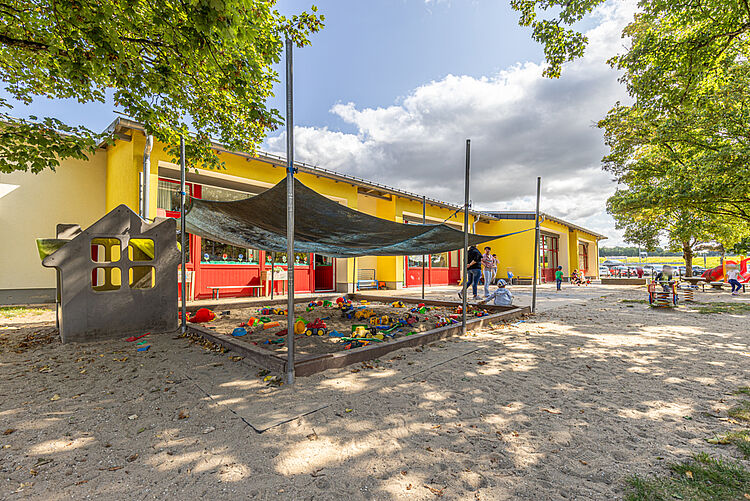 Sandkasten mit Spielzeug und Sonnenschutzplane im Außenbereich der Kita