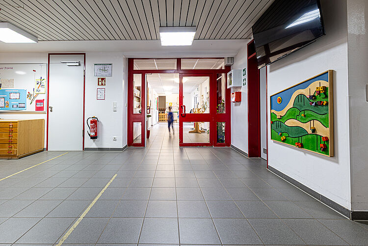Blick durch den hellen Flur der Kita mit Spielwand und roten Türen