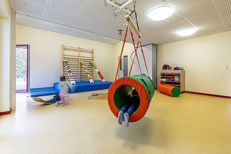 Kinder toben im Bewegungsraum der Kita mit Hängematte und Spielgeräten
