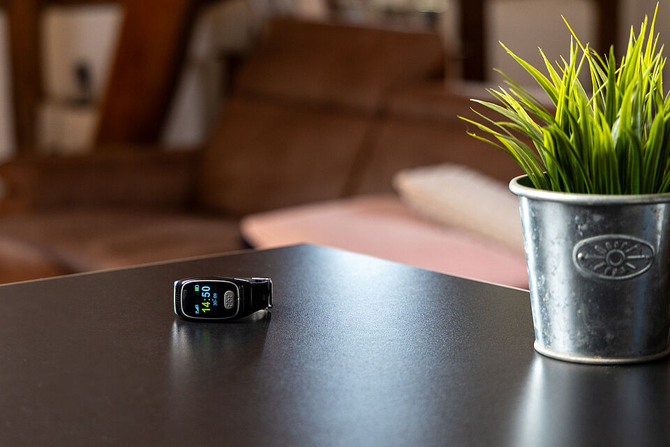 Schwarzes Notruf- oder Fitnessarmband liegt auf Tisch neben Pflanze