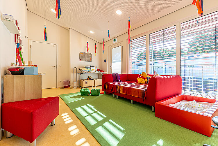 Kuscheliger Ruheraum und Bibliothek mit roten Sofas und Liegematten in der DRK-Kita „Henrys kleine Forscher“