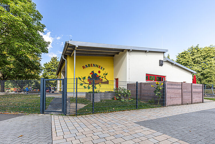 Außenansicht der DRK-Kita „Rabennest“ mit Wandlogo Gebäude der DRK-Kita „Rabennest“ mit farbenfroher Wandgestaltung und Zaun
