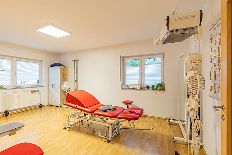 Physiotherapieraum mit roter Therapieliege und Skelettmodell