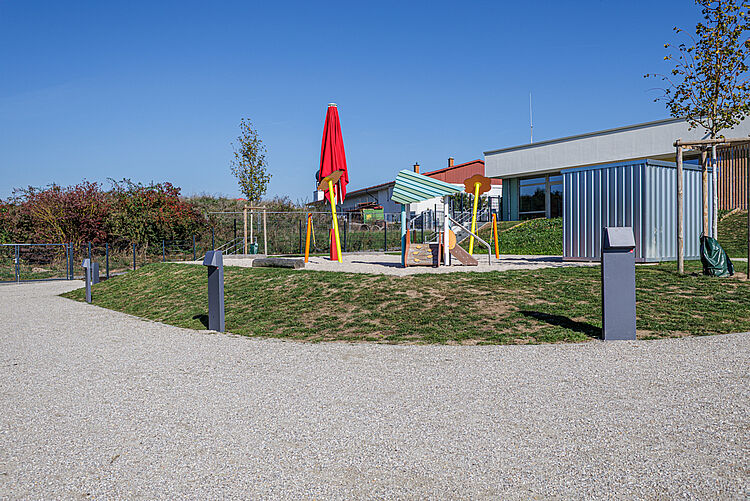 Kleiner Sandspielbereich mit Spielgerät, Sonnenschirm und Gerätehäuschen