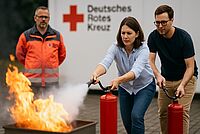 Zwei Teilnehmende der Brandschutzhelfer-Ausbildung beim Deutschen Roten Kreuz üben den Einsatz von Feuerlöschern unter Anleitung