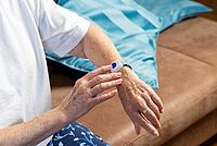 Seniorin mit DRK-Mobilruf-Armband drückt Notrufknopf am Handgelenk