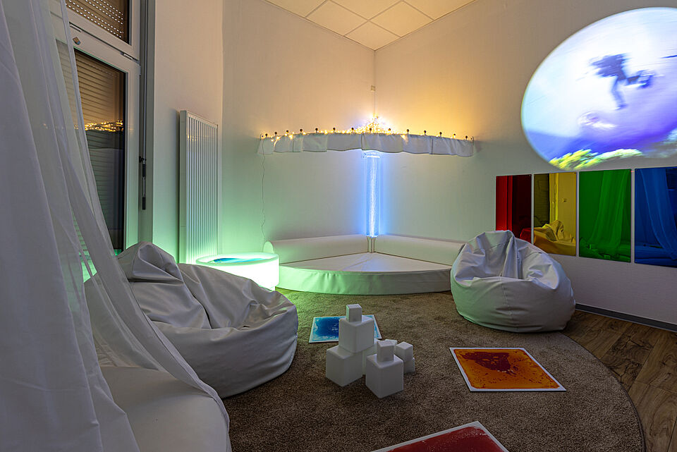 Weißer Snoezelenraum mit Lichtprojektionen, Sitzsäcken und Spiegelwand