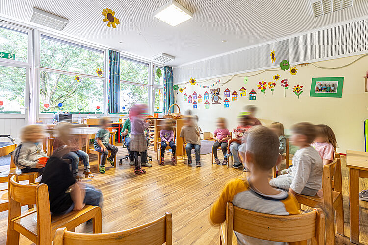 Kinder sitzen im Stuhlkreis und singen oder sprechen gemeinsam im Gruppenraum