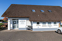 Eingangsbereich der DRK Physiotherapiepraxis in Pohlheim mit DRK-Fahrzeugen und Praxis-Schild