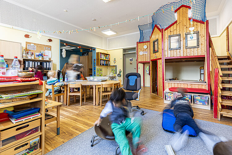 Kinder spielen in einem Gruppenraum mit Spielehaus und Basteltischen