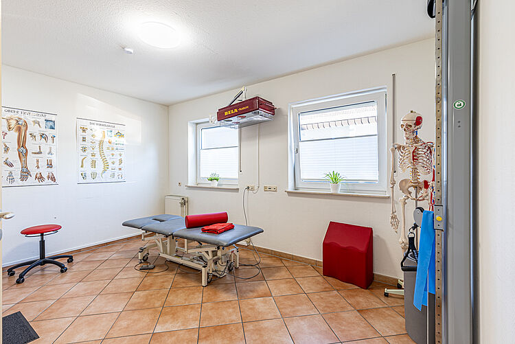 Behandlungsraum mit Therapieliege, Anatomiepostern und Skelettmodell