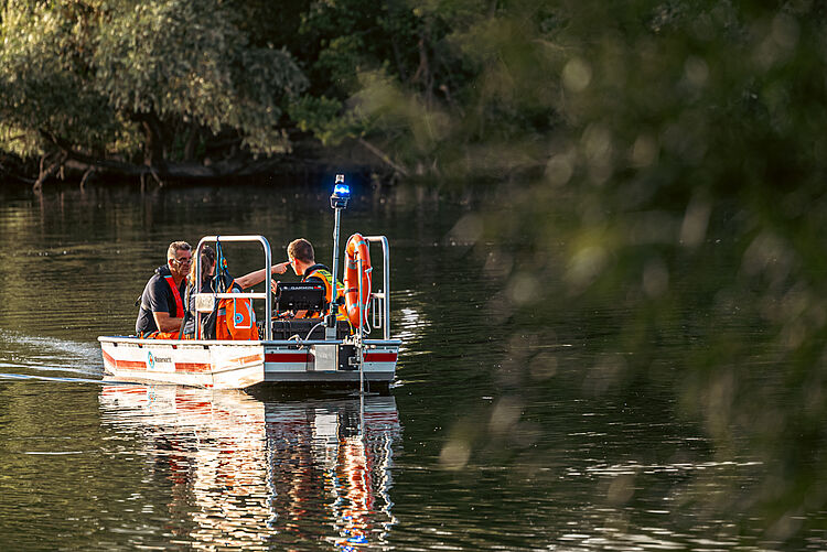 Wasserwacht-Team fährt mit Boot durch schattige Uferzone