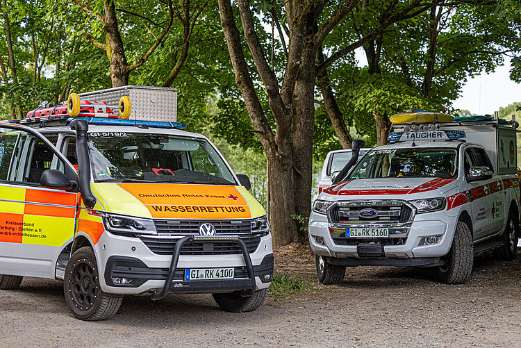 Einsatzfahrzeuge der DRK Wasserwacht und Wasserrettung im Schatten von Bäumen
