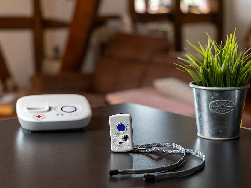 Hausnotrufgerät mit Notrufsender und rotem Kreuz auf einem Tisch