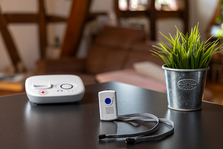 Hausnotrufgerät mit Notrufsender und rotem Kreuz auf einem Tisch