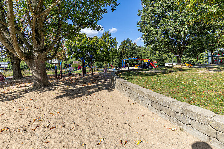 Sandspielfläche mit Bäumen und Spielgeräten im Außenbereich