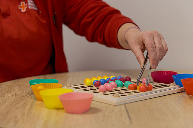 Ergotherapeutische Feinmotorikübung mit bunten Kugeln und Pinzette