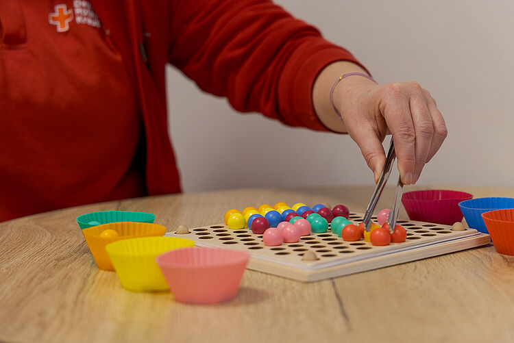 Ergotherapeutische Feinmotorikübung mit bunten Kugeln und Pinzette